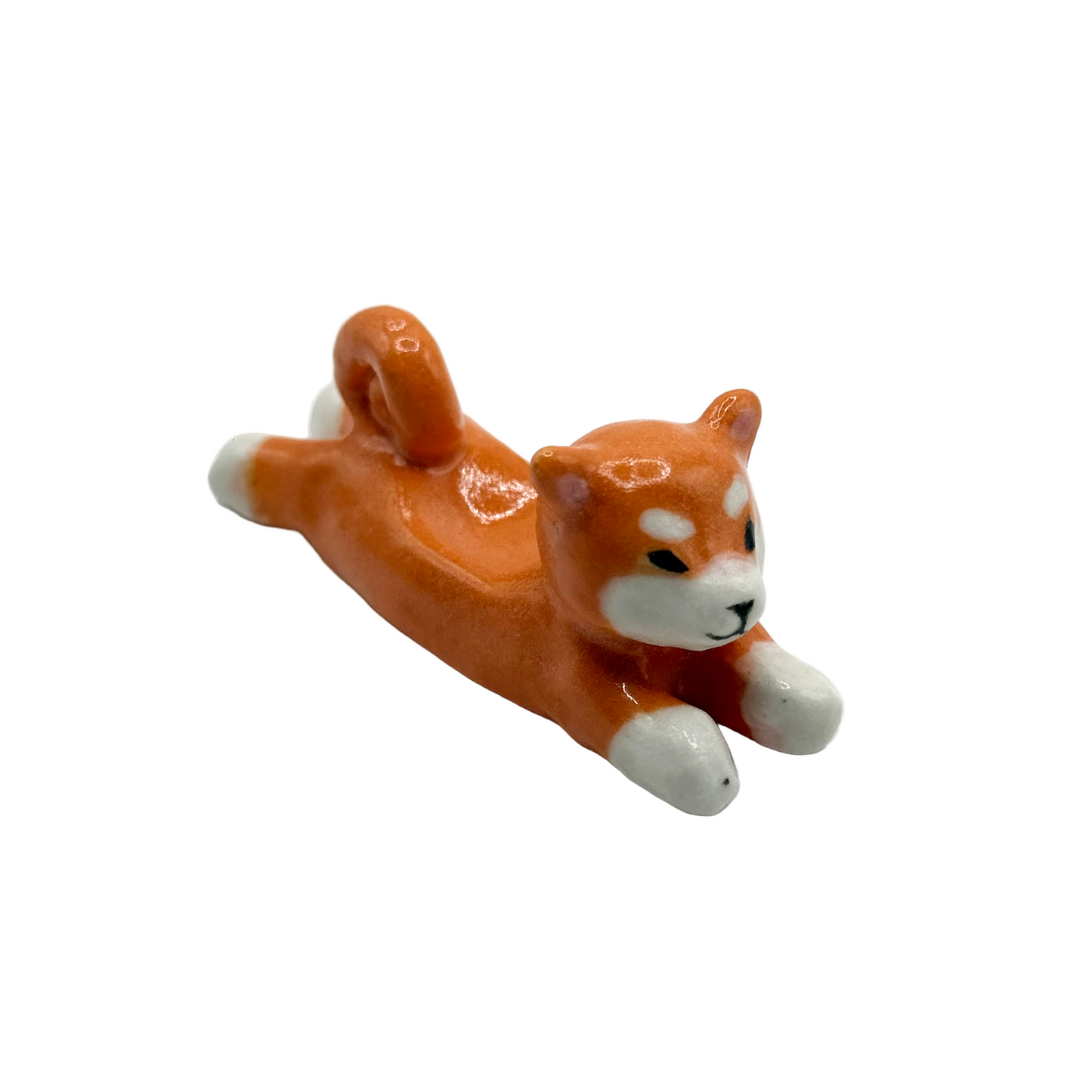 Small figurine of a lying dog with orange fur and white paws on a white background